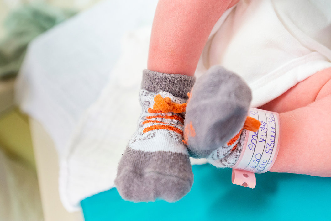 Neugeborenes Baby trägt graue Socken mit Tiger-Motiv und ein Krankenhausarmband am Bein